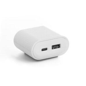A white, rectangular dual-port wall charger with rounded edges and a ribbed, matte texture on its main body. The front face is a smooth, glossy oval featuring one USB-C port and one USB-A port. The device is angled on a plain white surface, casting a soft shadow to the left.