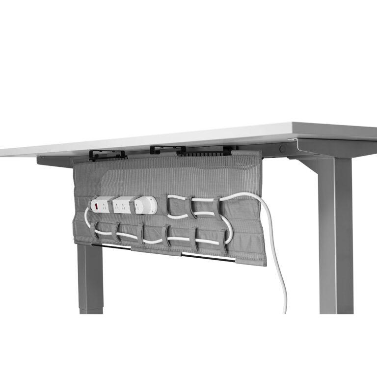 A gray mesh cable management tray is shown in an "open" or "down" position, hanging vertically from black brackets underneath a white desk. The interior of the tray features several horizontal fabric loops used to organize and secure a white power strip and coiled power cables against the mesh backing. This design allows for easy access to wiring while maintaining a tidy workspace. The desk is supported by silver square-post legs against a plain white background.