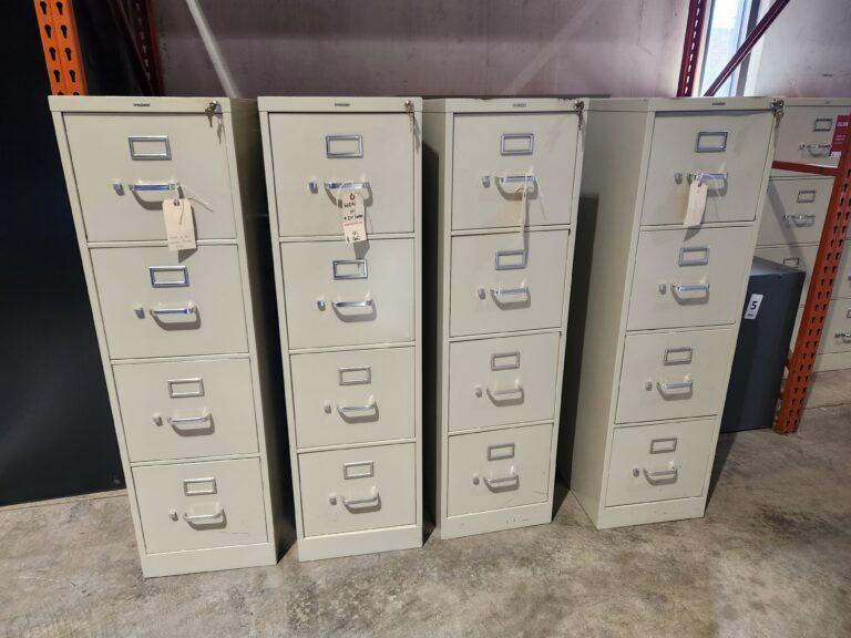 Four beige HON 4-drawer vertical locking letter file cabinets with silver handles and label holders arranged in a row on a concrete warehouse floor.