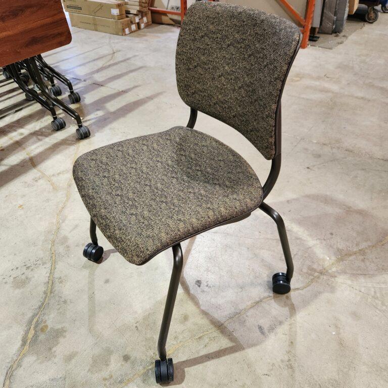 A side-view of a rolling stacking chair with olive and black patterned fabric upholstery, a dark metal frame, and four black casters on a concrete floor.