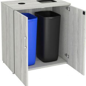 A double-stream waste and recycling cabinet is shown with its doors open to reveal two large plastic bins. The cabinet features a light gray wood-grain laminate finish. The top of the cabinet has two separate disposal openings: a circular one on the left for recyclables and a larger rectangular one on the right for general waste. Inside, the unit holds a tall blue bin, typically used for recycling, and a tall black bin for trash. The cabinet doors are equipped with silver horizontal handles and heavy-duty hinges.
