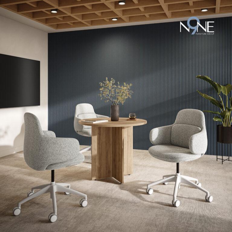 Three Viva chairs with light gray textured upholstery and white wheeled bases are positioned around a round, light wood pedestal table in an office setting with a blue-gray ribbed wall and a wood-slatted ceiling.