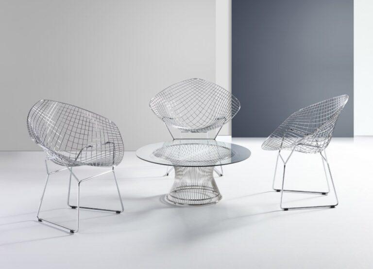 A Santana coffee table with a glass top and chrome wire base centered between three chrome wire diamond-style lounge chairs in a white and gray studio setting.